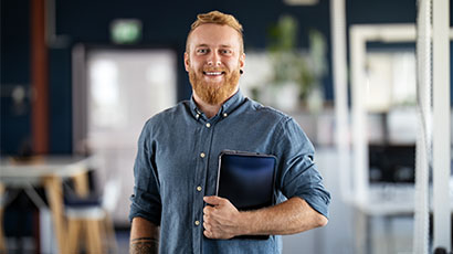 Man in blue shirt holding case and smiling, confidently to camera.