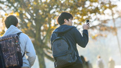 Two students on campus, one with a phone in his hand