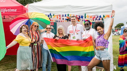 UWE Bristol staff members standing in front of a rainbow flag at Bristol Pride.