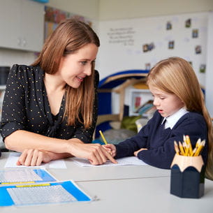 A female teacher with a young student, who is writing on a sheet of paper