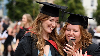 Two graduates at graduation looking at a phone
