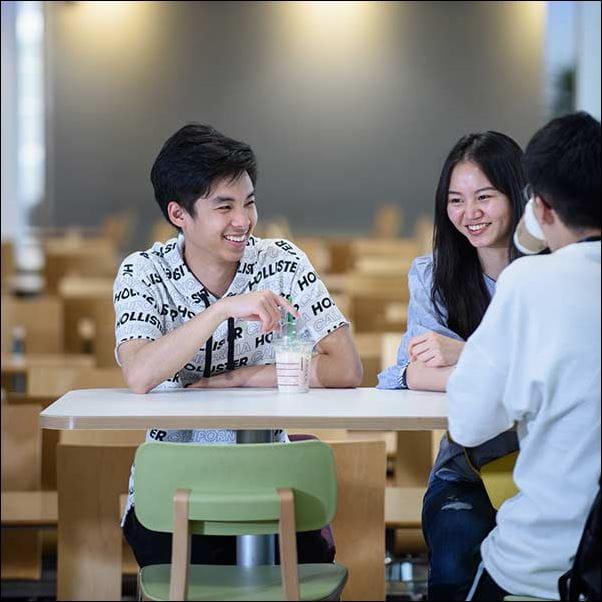 A group of international students, laughing with each other whilst sat around a table.