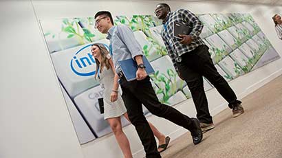 Three smiling placement students walking down the corridor at the Intel office as they hold netbooks under their arms.
