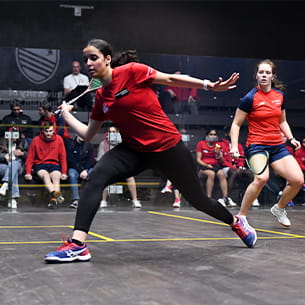 Performance sport athlete on a squash court lunging forward with a squash racket ready to hit the ball.