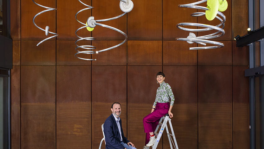 Alice Channer and Professor Ioannis Ieropoulos on a ladder with her 'Nanowires' sculpture in the Engineering Building. Photo credit: Thierry Bal, 2021.