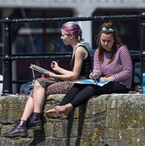 Two students sitting on the edge of the Bristol harbourside drawing the surrounding landscape.