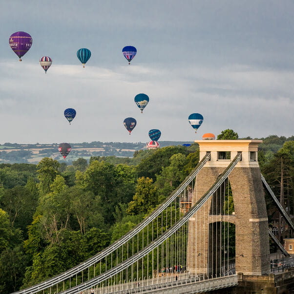 Hot air balloons ascend with Clifton Suspension Bridge in foreground.
