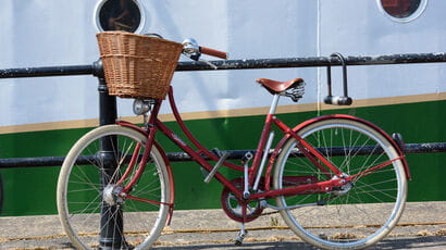 Red bike with wicker basket leaning against railings in front of a white and green barge.