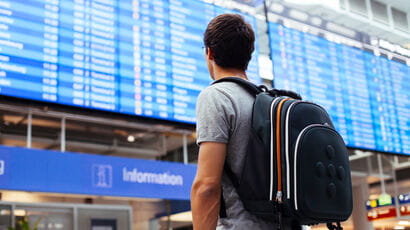 Student at the airport looking up at the departure board.