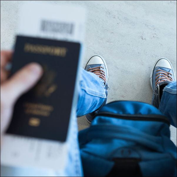 Close up of a passport, backpack and feet in trainers
