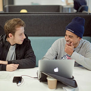 Two students talking whilst using a laptop