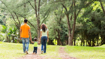 Parents walking with their child on a woodland path.