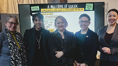 Five women smiling for a photo in front of a digital whiteboard that says 'A New Crime of Ecocide'