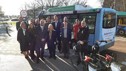 Group of people in suits standing in front of automated zero emissions bus smiling to camera