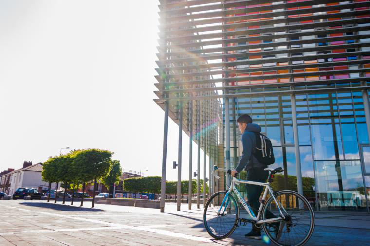 A student pushes a bicycle in front of a modern building.