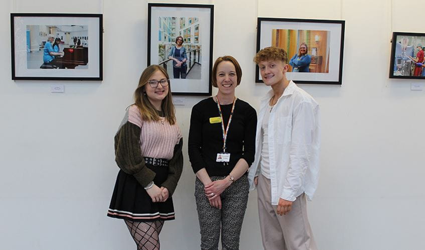 Students Carla Mabb and  Kian Swainston, with arts programme manager Donna Baber standing in front of the photography exhibition at the Brunel building