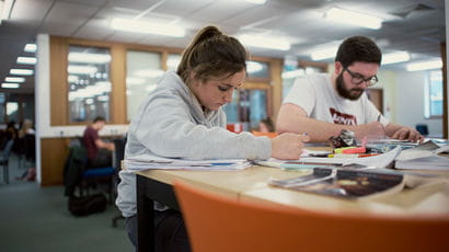Two students working at a desk in the Library