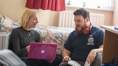 Two students smiling with a laptop and textbook in student accommodation