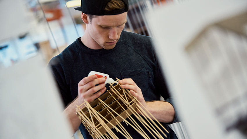 A student assembling a small wooden building model
