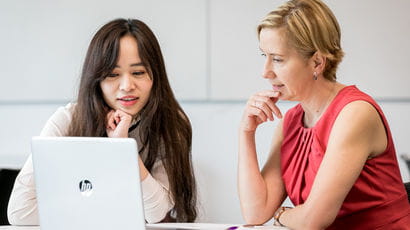 Student with a laptop talking to a member of staff