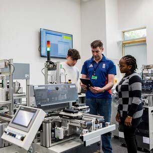 Two students being shown how to work a piece of equipment by a technician.