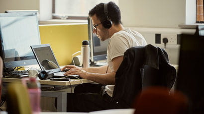 A student with headphones on, working on a laptop