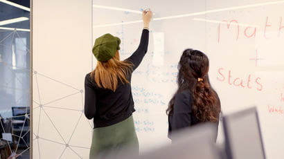 Two people drawing on the board in a maths room.