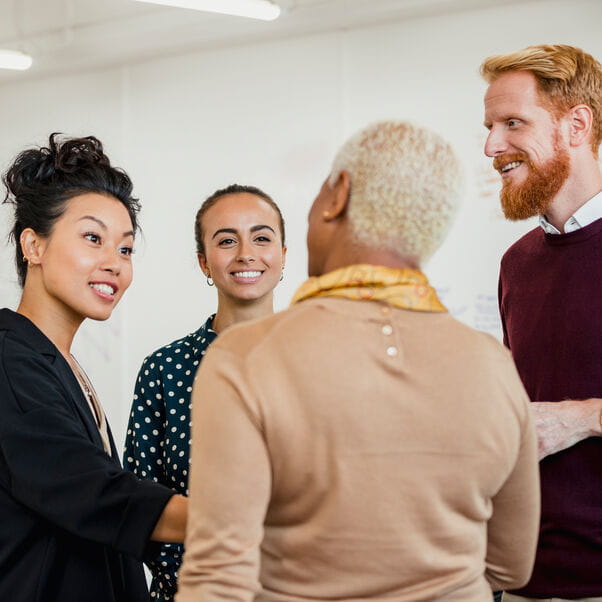 Team of staff standing and talking in an office environment.