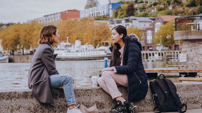 Two female students sitting on a wall on the Bristol Harbour.