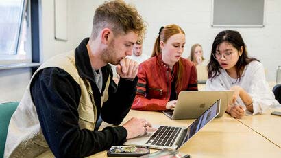 A group of students sat at a table looking at their laptops.