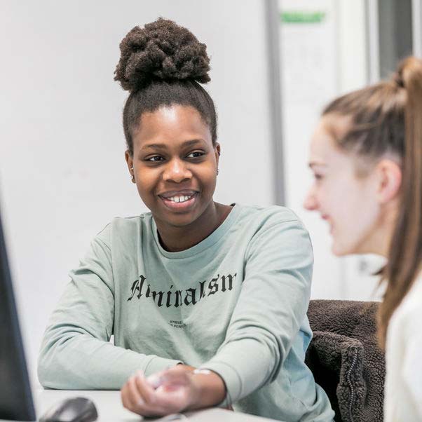 A couple of students chatting next to a computer