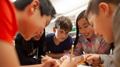A group of young children at school sitting around a table together working on a project.