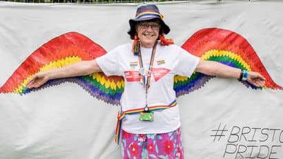 UWE Bristol staff member standing in front of a rainbow flag at Bristol Pride.