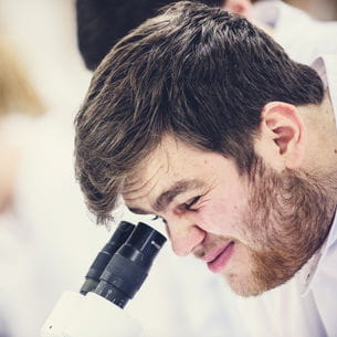 A student looking intently into a microscope.