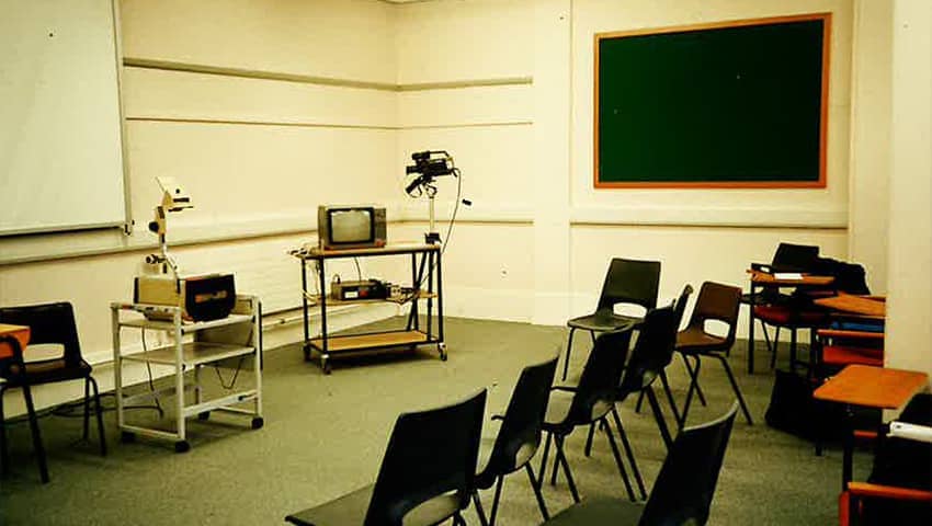 A 1990s classroom with overhead projector, a small television and a chalk board.