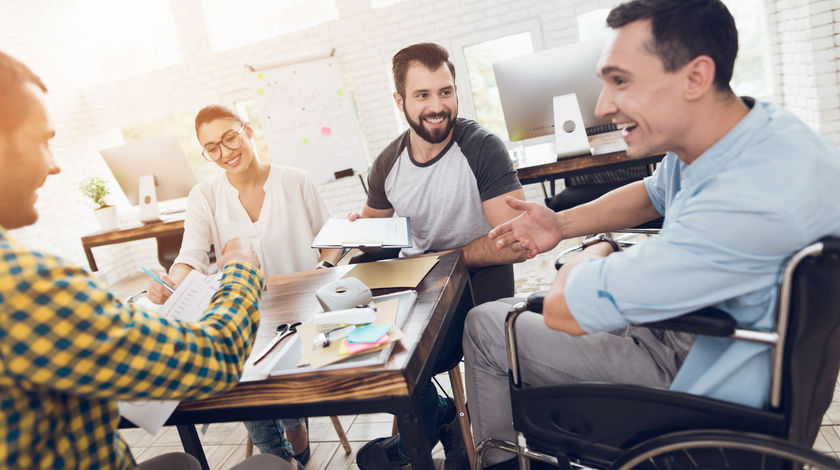 Wheelchair user sat with colleagues at a table during a meeting.