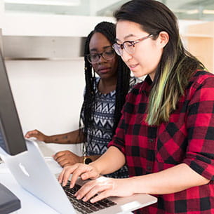 Two women working on laptops in an office.