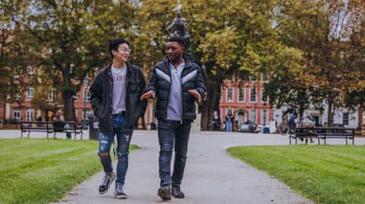Two male students walking through a park.