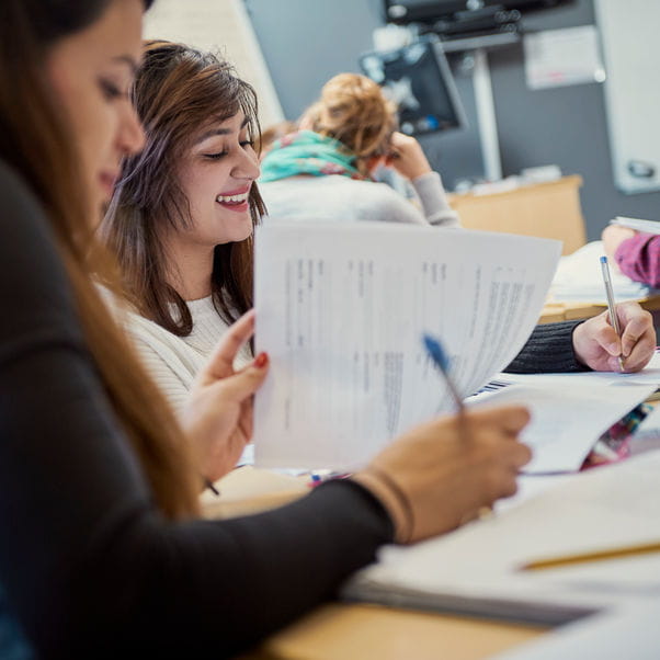 Two students working at a desk, focus is on one student who is smiling