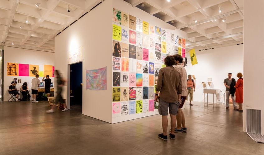 Degree show guests looking at a full gallery wall of student work 