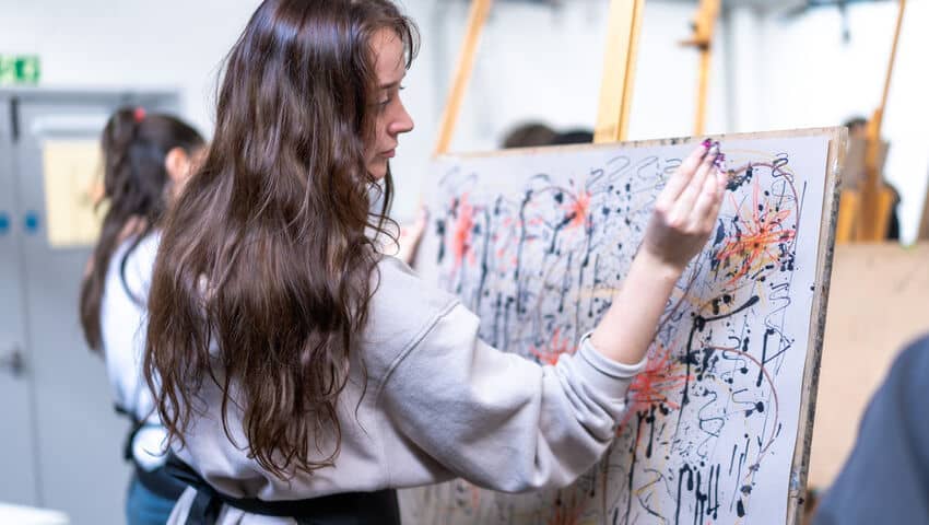 Student creating mixed media art piece on canvas as part of Drawing Week