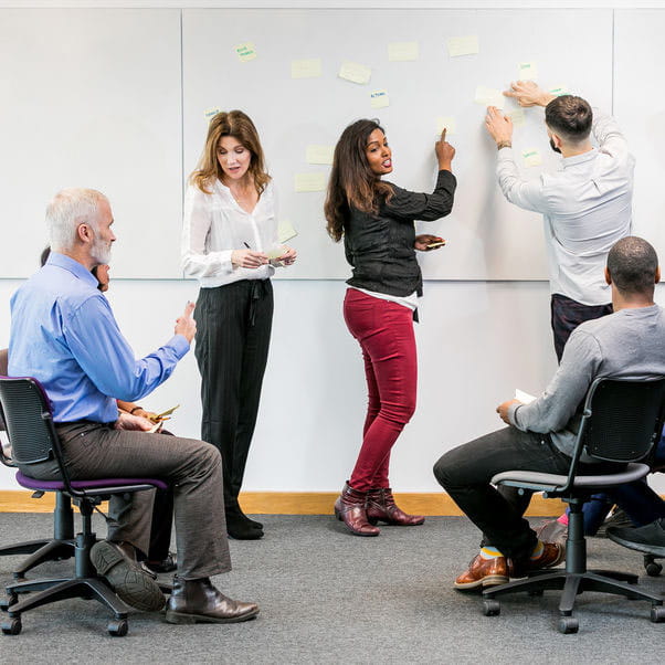 Staff writing on a whiteboard in front of colleagues.