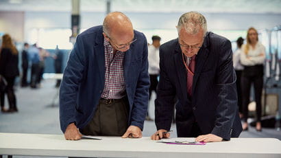 A couple of mature males reading notes on a clipboard