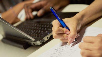 close up of someone writing notes next to a laptop