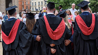 A photograph taken from behind of four students at graduation