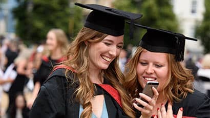 Two graduates at graduation looking at a phone