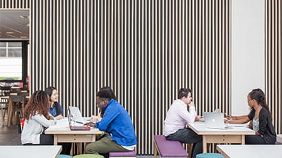 Students sat chatting, while looking at laptops, in the Atrium at UWE Bristol Business school