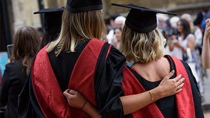 Back-shot of two graduates posing for a photo with their arms around eachother