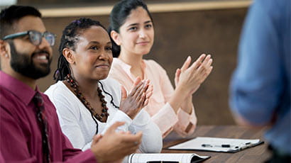 Three people sat at a desk clapping