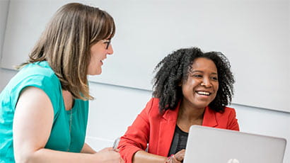 Two women sat looking at a laptop, laughing